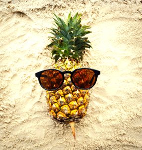 A pineapple with sunglasses on a beach