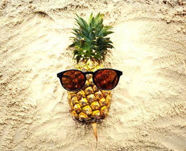 A pineapple with sunglasses on a beach