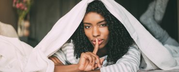 attractive black woman asking for silence with finger on lips on bed