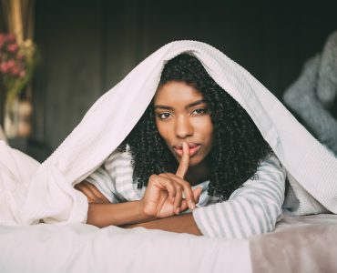 attractive black woman asking for silence with finger on lips on bed