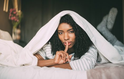 attractive black woman asking for silence with finger on lips on bed