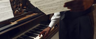 Black pianist with music notebook in his hands on the stage with spotlights on background. Negro performer poses at musical instrument before concert