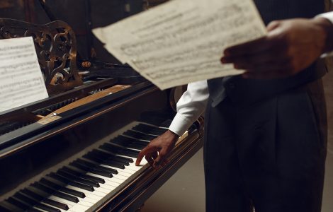 Black pianist with music notebook in his hands on the stage with spotlights on background. Negro performer poses at musical instrument before concert