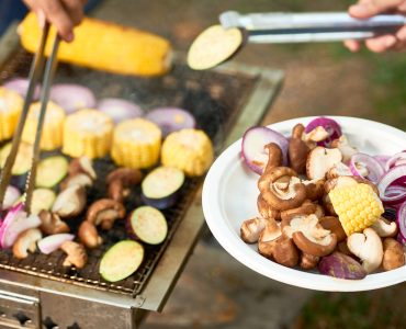 Close-up of woman holding plate with ready vegetables while man cooking the other vegetables on the grill outdoors