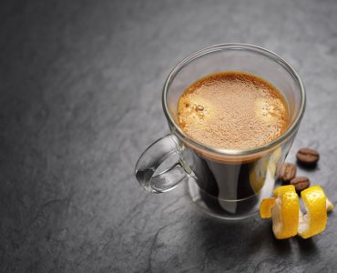 Transparent double wall glass espresso coffee mug with lemon peel on black slate background