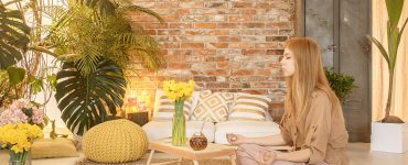 Young girl meditating in cozy natural room with red brick wall