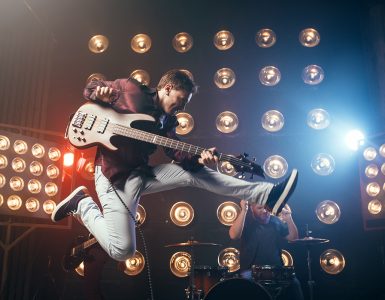 Guitarist plays on bas-guitar, snapshot in a jump, stage with lights on background. Rock band concert