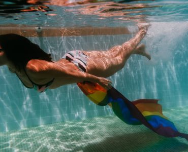 young woman in a pool holding rainbow gay flag underwater.LGBTQ concept. Summertime