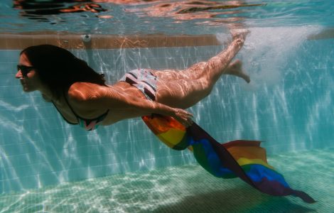 young woman in a pool holding rainbow gay flag underwater.LGBTQ concept. Summertime