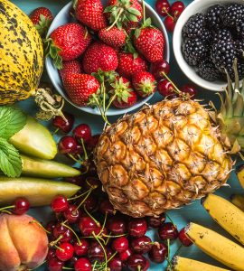 Healthy summer fruit variety. Sweet cherries, strawberries, blackberries, peaches, bananas, melon slices and mint leaves on blue backdrop. Top view