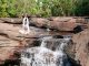 woman in white practicing awareness yoga next to waterfall cascading from red rocks