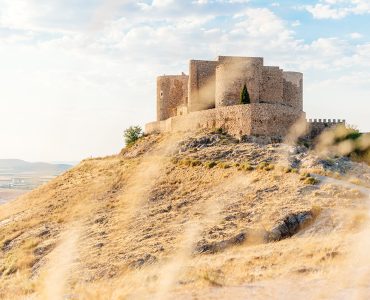 Romanesque castle on top of a hill with dry bush branches out of focus in foreground in Consuegra, Toledo, Spain