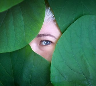 Female eye behind big green leaves