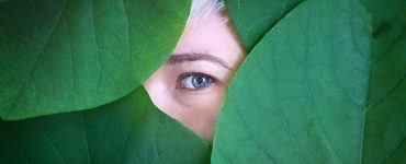 Female eye behind big green leaves