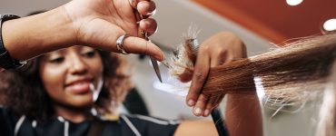 Close-up image of smiling hairdresser cutting split ends of section of hair