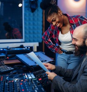 Sound operator and female singer at remote control panel in audio recording studio. Musician at the mixer, professional music mixing