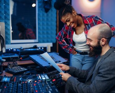 Sound operator and female singer at remote control panel in audio recording studio. Musician at the mixer, professional music mixing