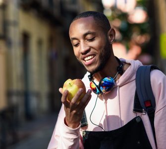 Young black man eating an apple walking down the street. Lifestyle concept.