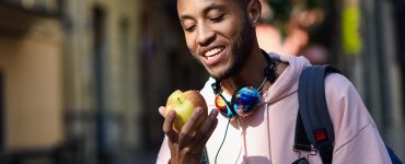 Young black man eating an apple walking down the street. Lifestyle concept.